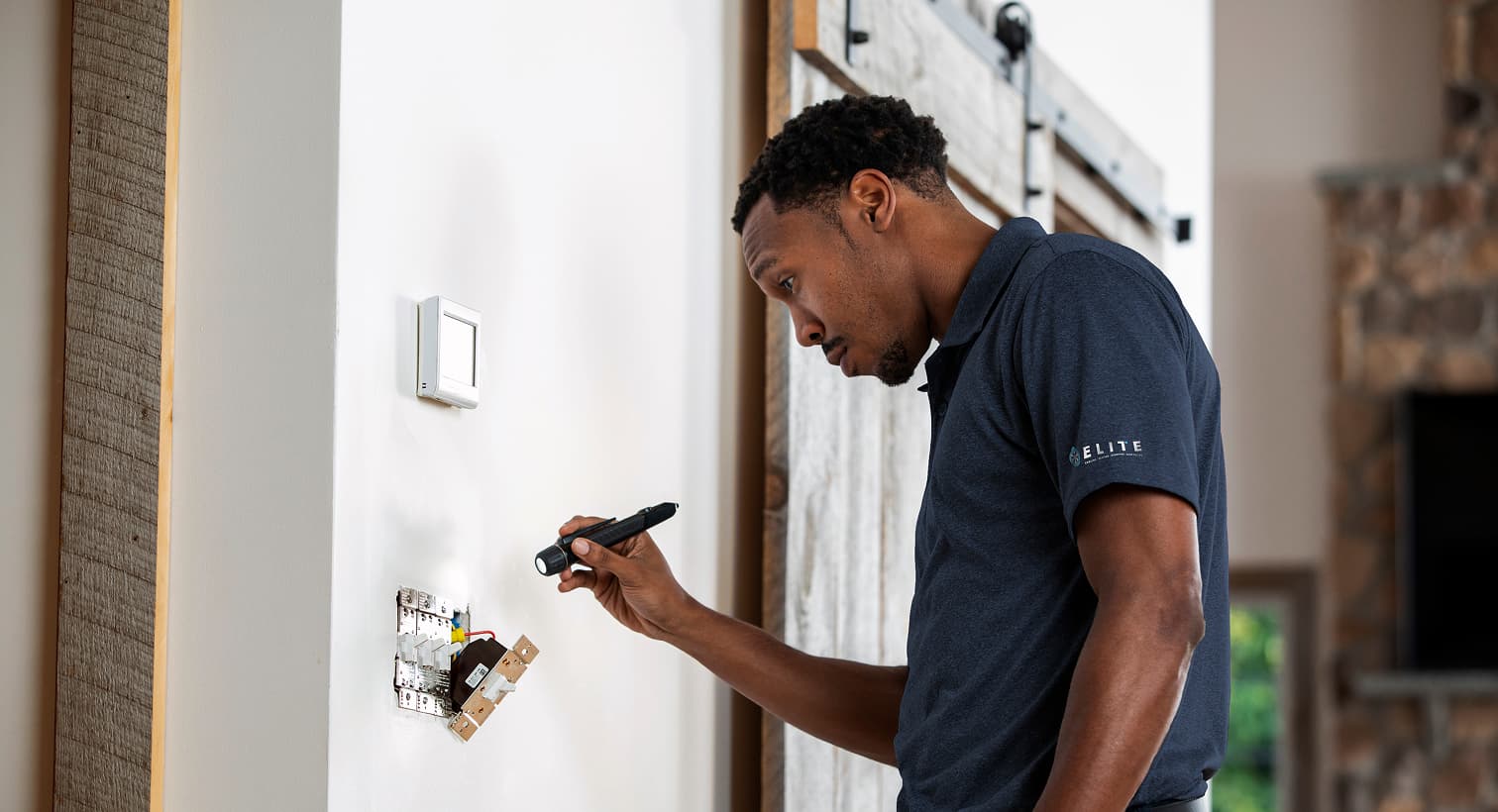 A professional Elite electrician using a flashlight to safely inspect and troubleshoot exposed residential wall switch wiring during an electrical repair service.