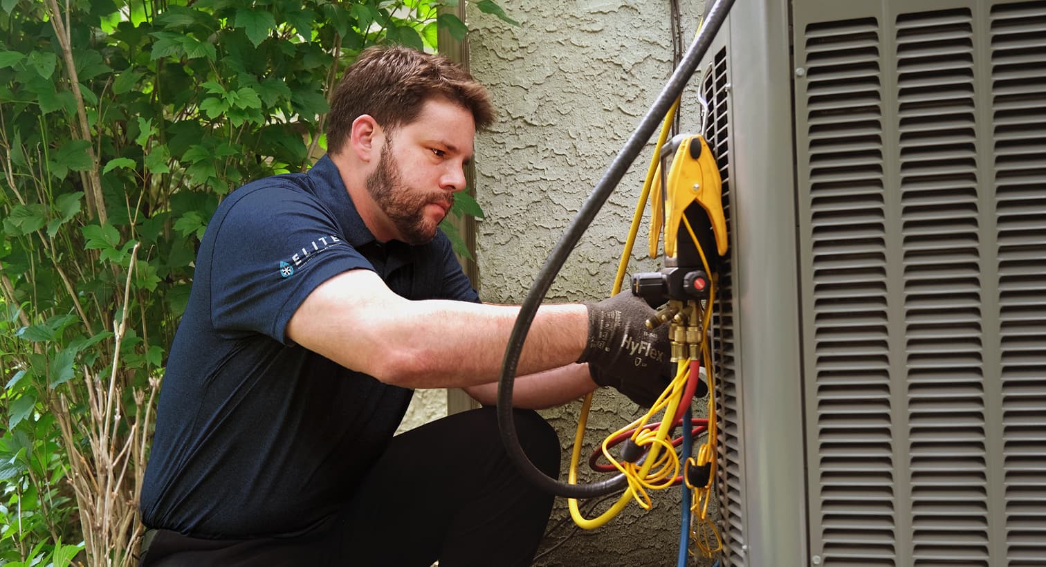 A professional Elite HVAC technician inspecting an outdoor central air conditioning unit to provide residential AC repair and diagnostic services.