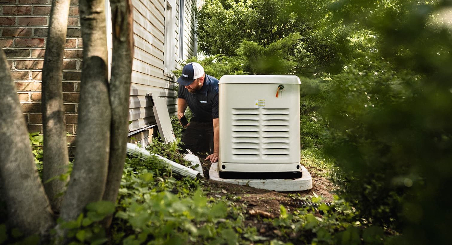 A professional Elite technician inspects a large, beige whole-home standby generator installed on a concrete pad outside a residential house.