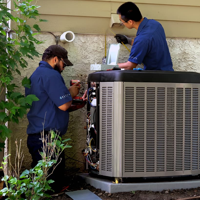 Two Elite HVAC technicians installing a brand-new residential outdoor air conditioning condenser unit during a home AC replacement service.